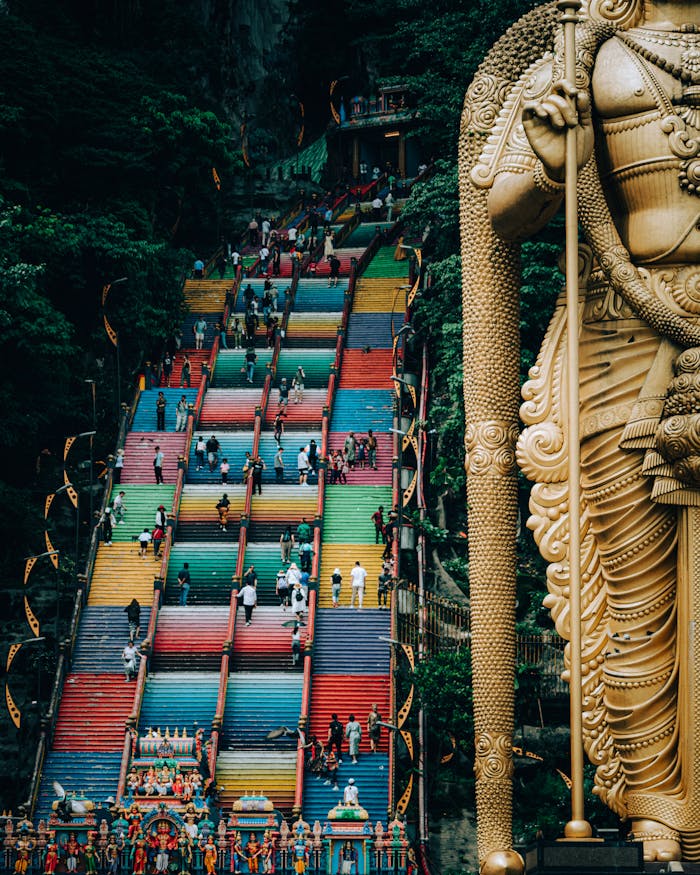 Vibrant staircase leading to Batu Caves with iconic statue and visitors ascending.