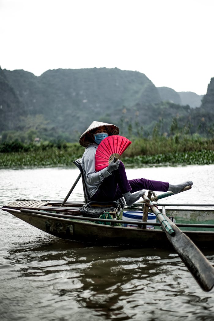 Person wearing a conical hat rowing a sampan on a river in Vietnam, showcasing local culture.