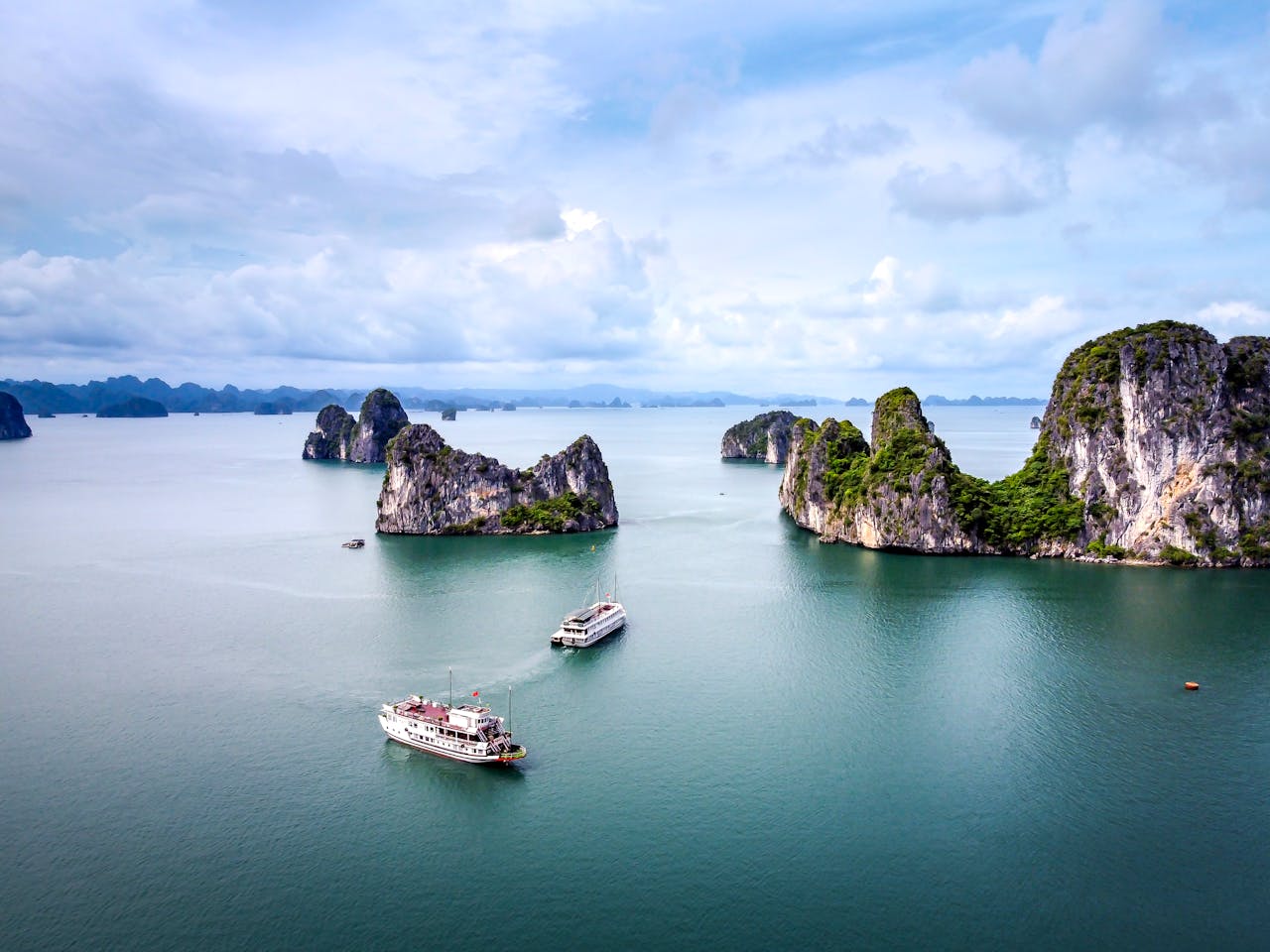 Stunning aerial view of Halong Bay's limestone islands and cruise ships on a cloudy day.